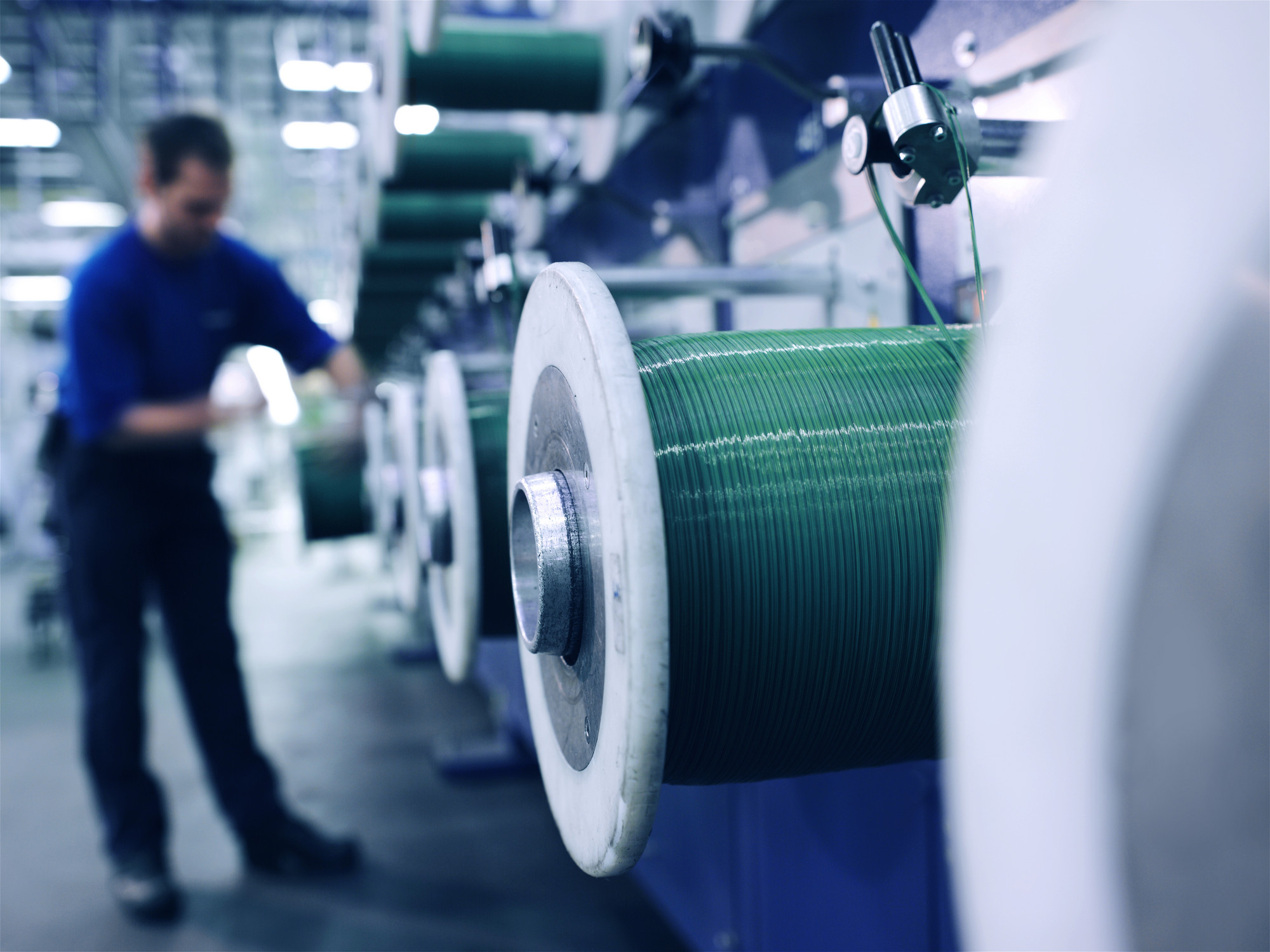 Worker operating a large industrial yarn-winding machine inside a manufacturing facility.