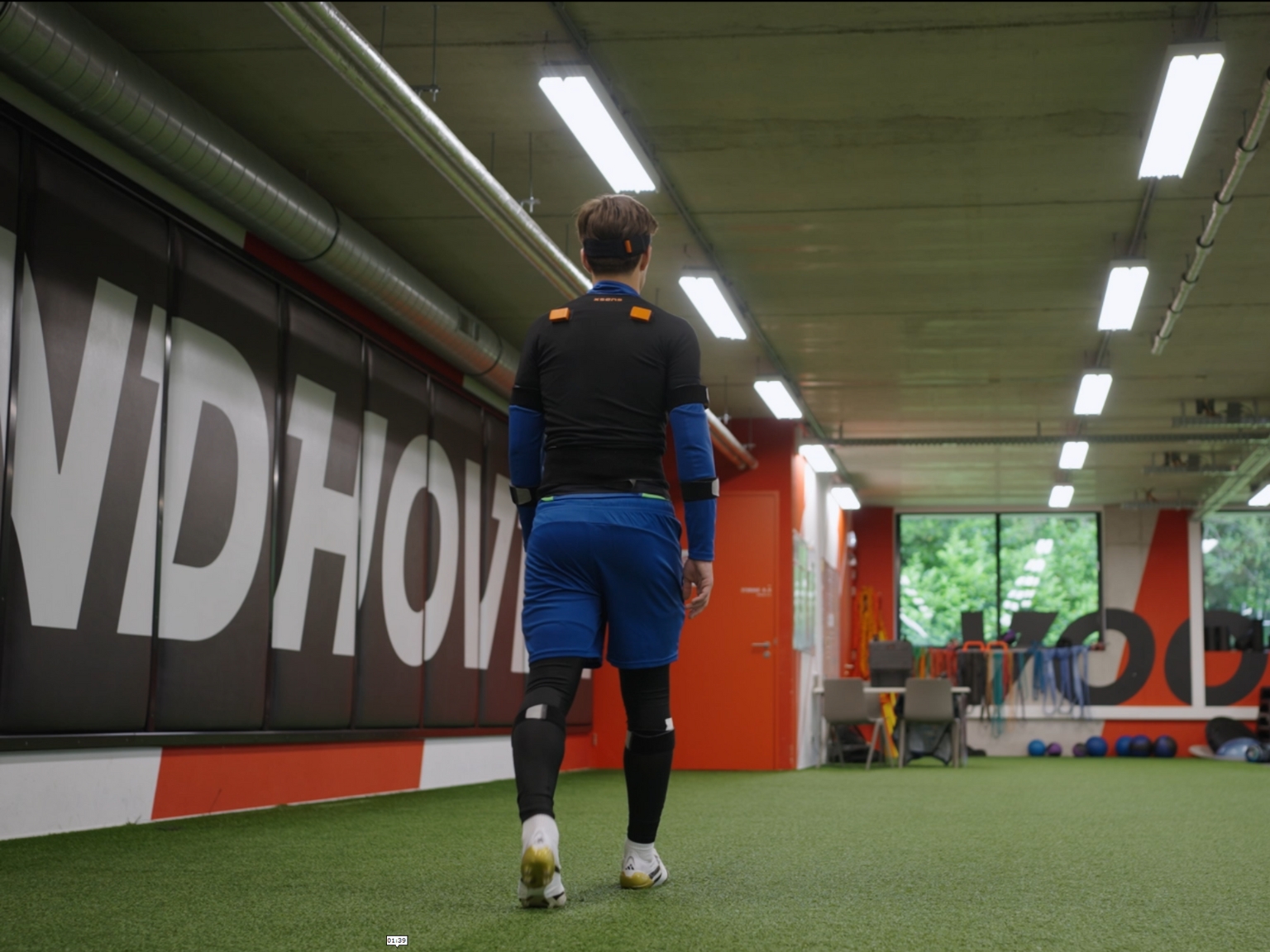 Athlete walking across an indoor artificial turf testing area while wearing motion sensors.