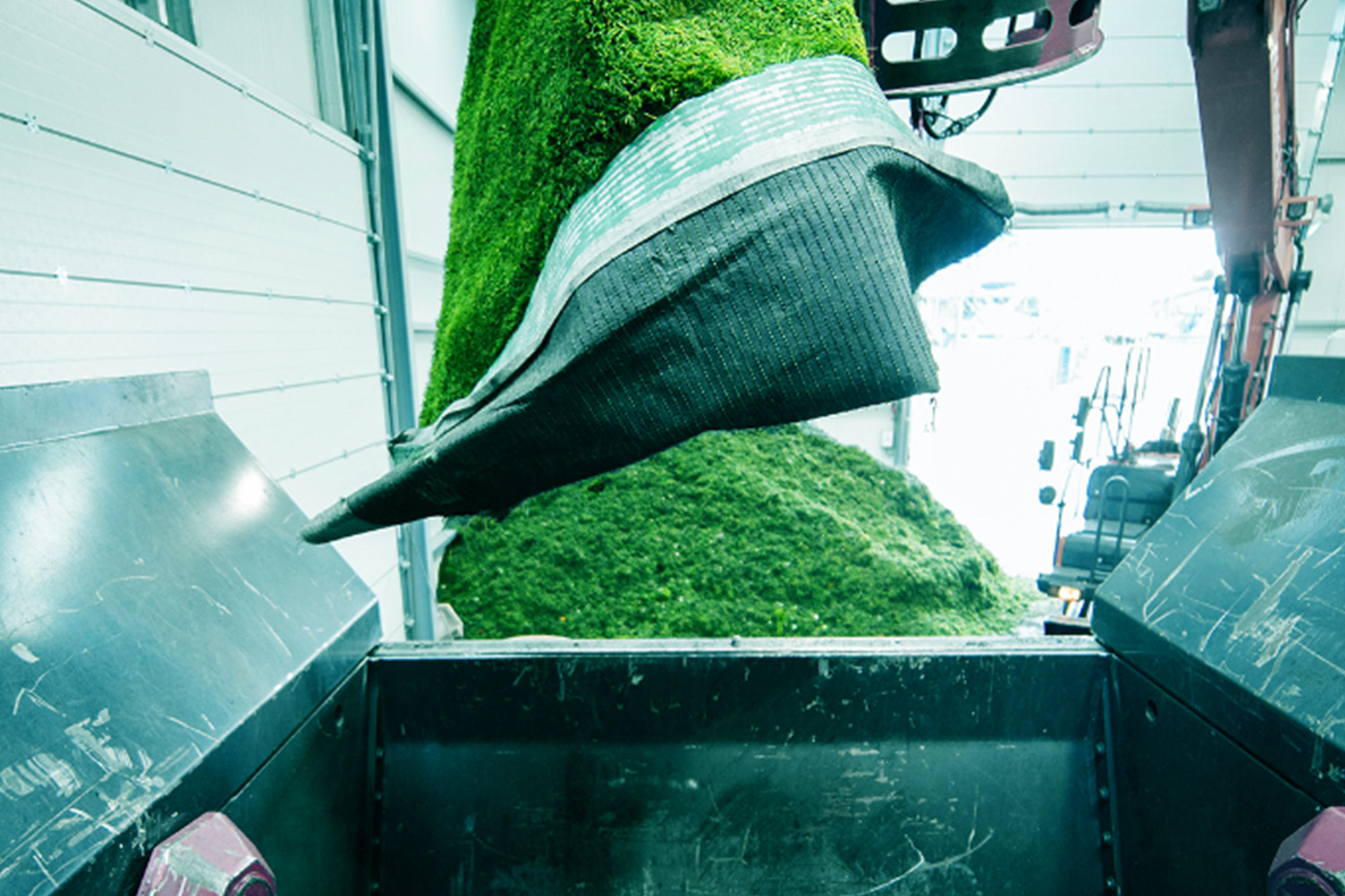 Piece of used artificial turf being lifted and dropped into an industrial recycling machine.