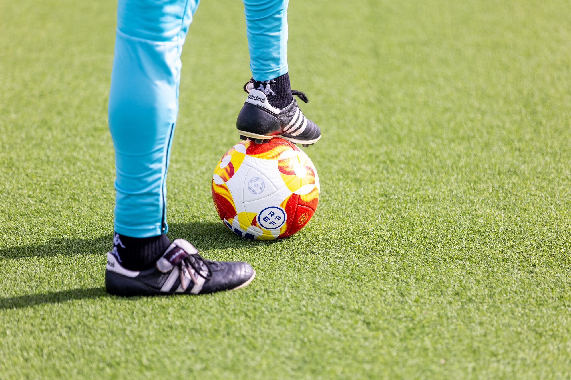 foot placed on football on artificial pitch