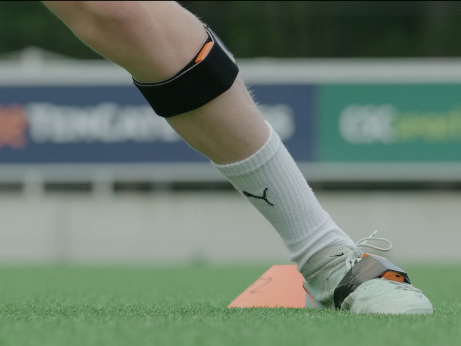 Close-up of football boots fitted with motion-tracking sensors on artificial turf.
