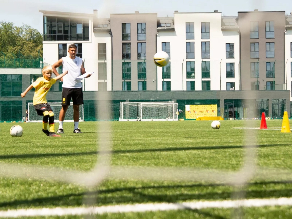 Child practicing soccer on an artificial turf field with a coach observing, cones and balls placed around for training.