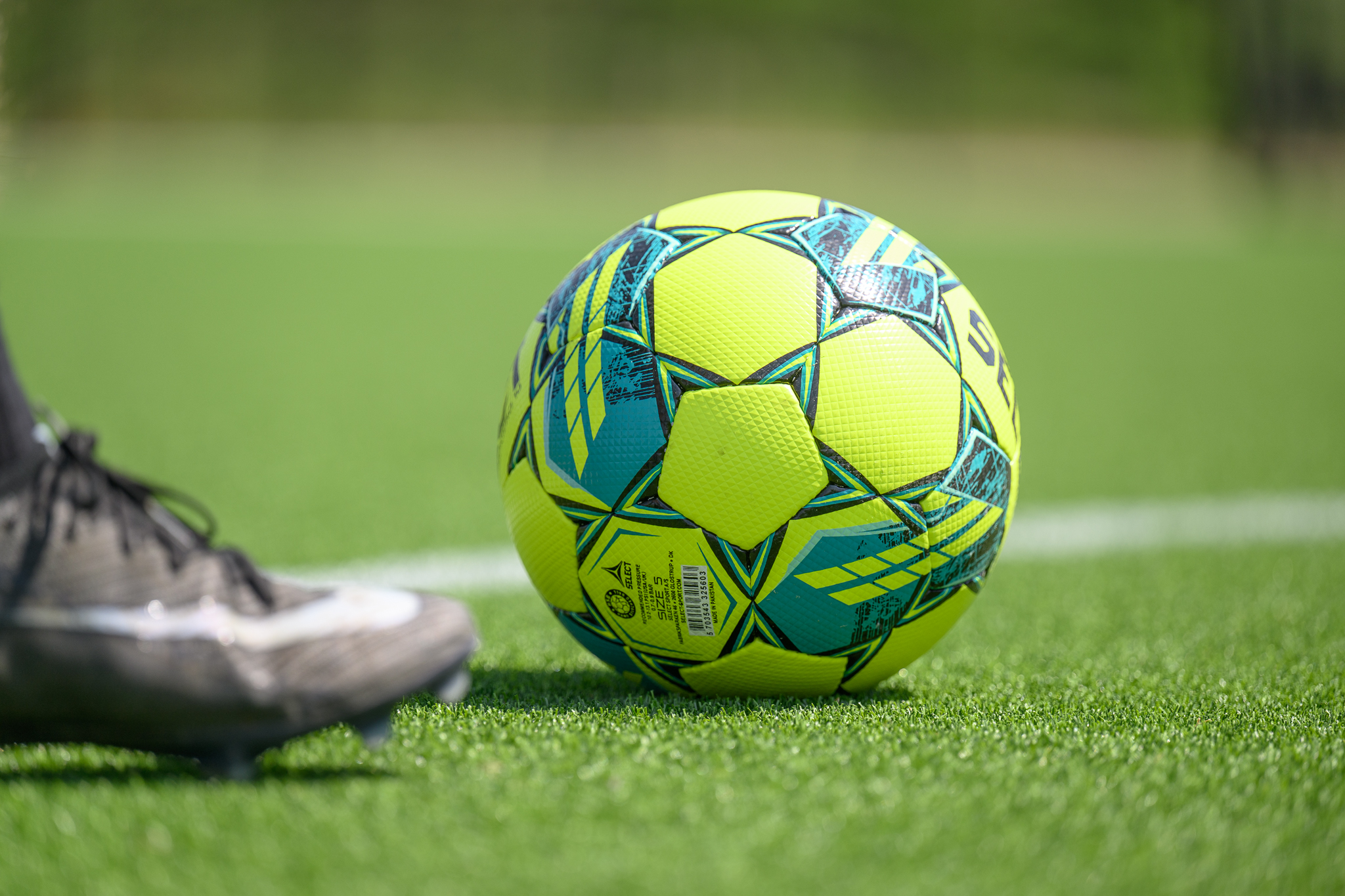 Close up ball image on artificial turf with boot coming from the left