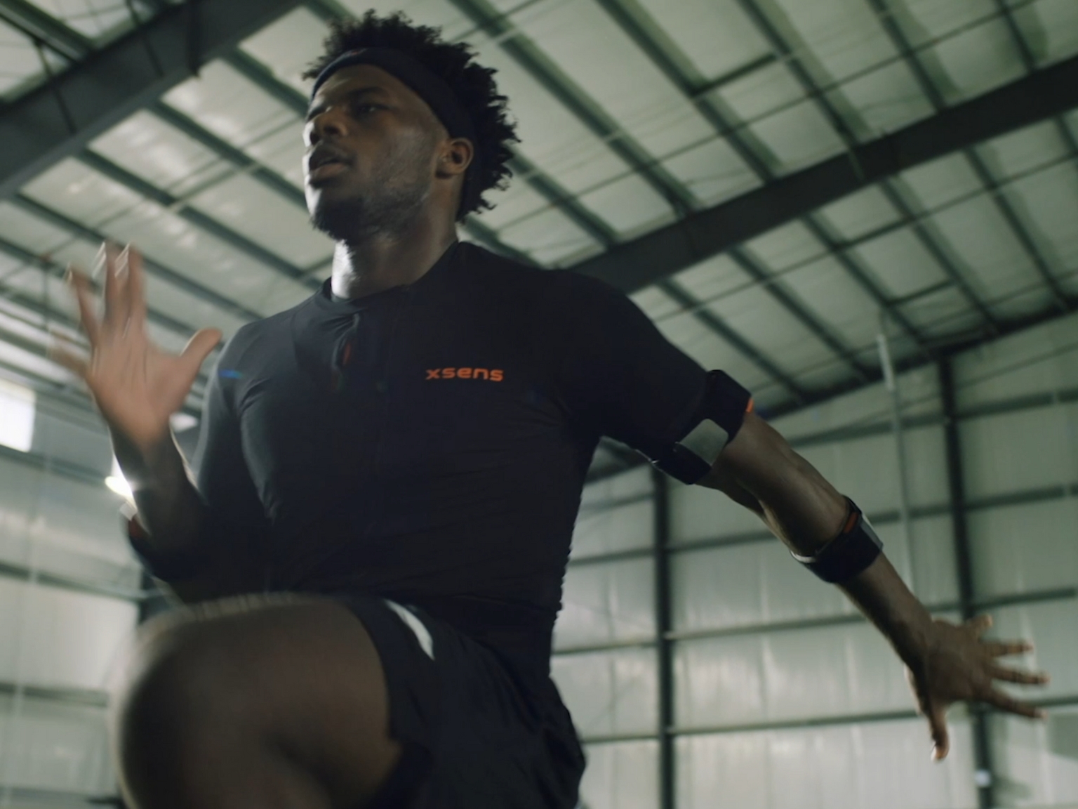 Athlete performing a high-knee running drill indoors while wearing motion-tracking sensors.