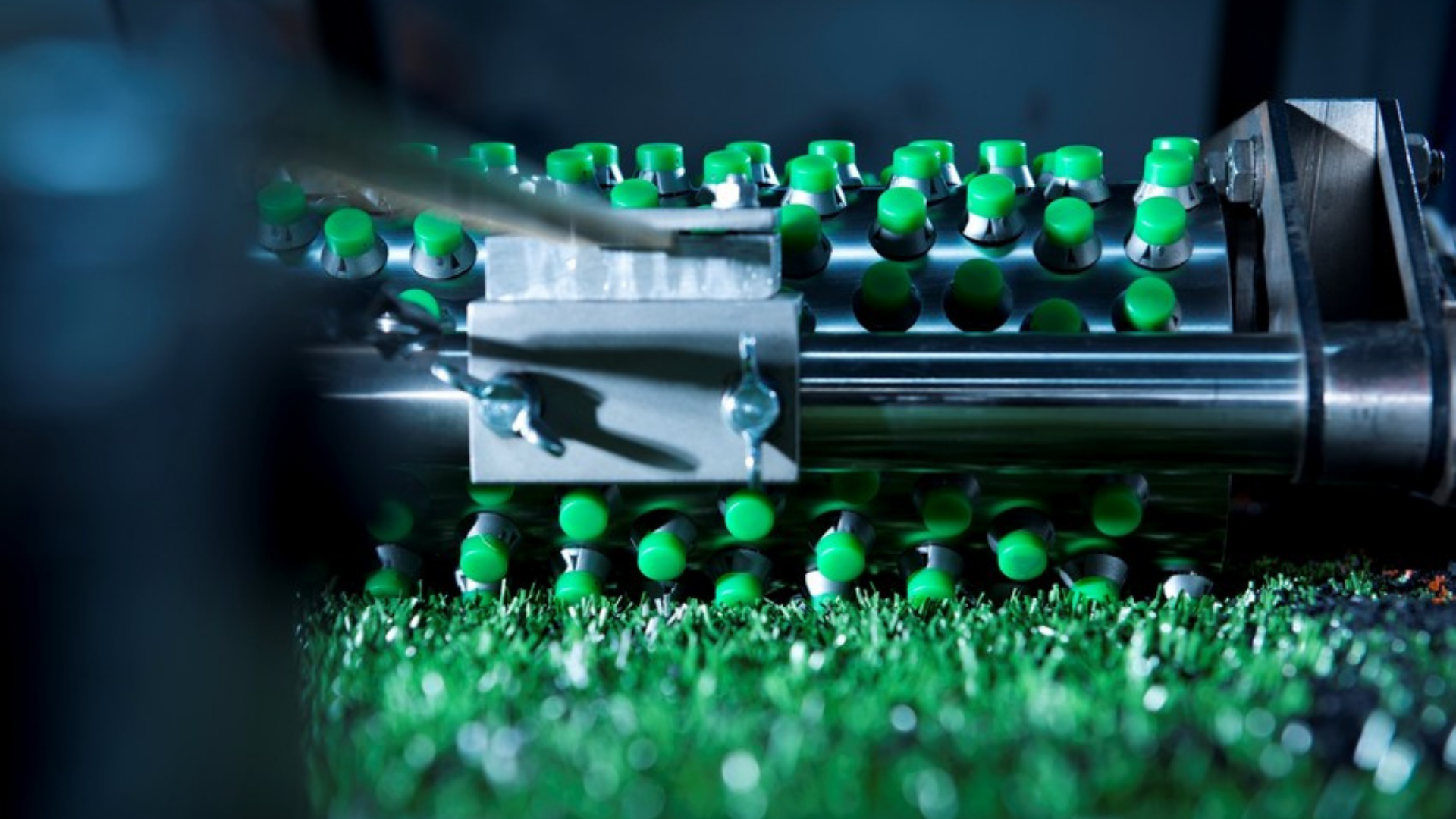 Close-up of a machine with multiple green-tipped metal pins pressing into artificial turf during a durability test.